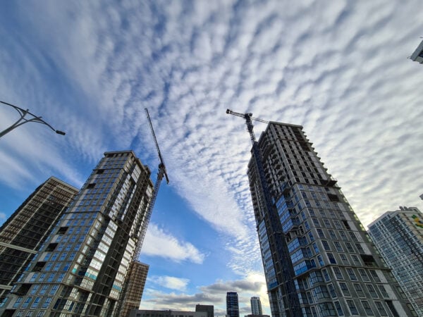 Multi-storey_buildings_under_construction_with_tower_cranes_against_background_of_blue_sky_with_clouds