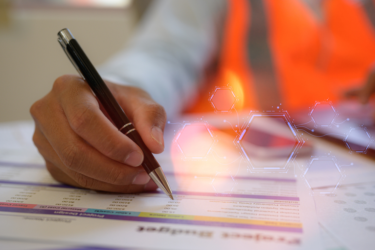an engineer or foreman working on site sitting on desk in office using pen and computer analysing data charts paper work